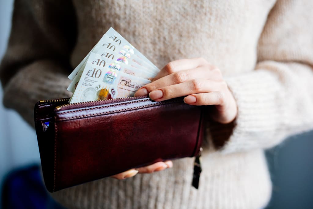 Person holding £10 notes in a brown wallet